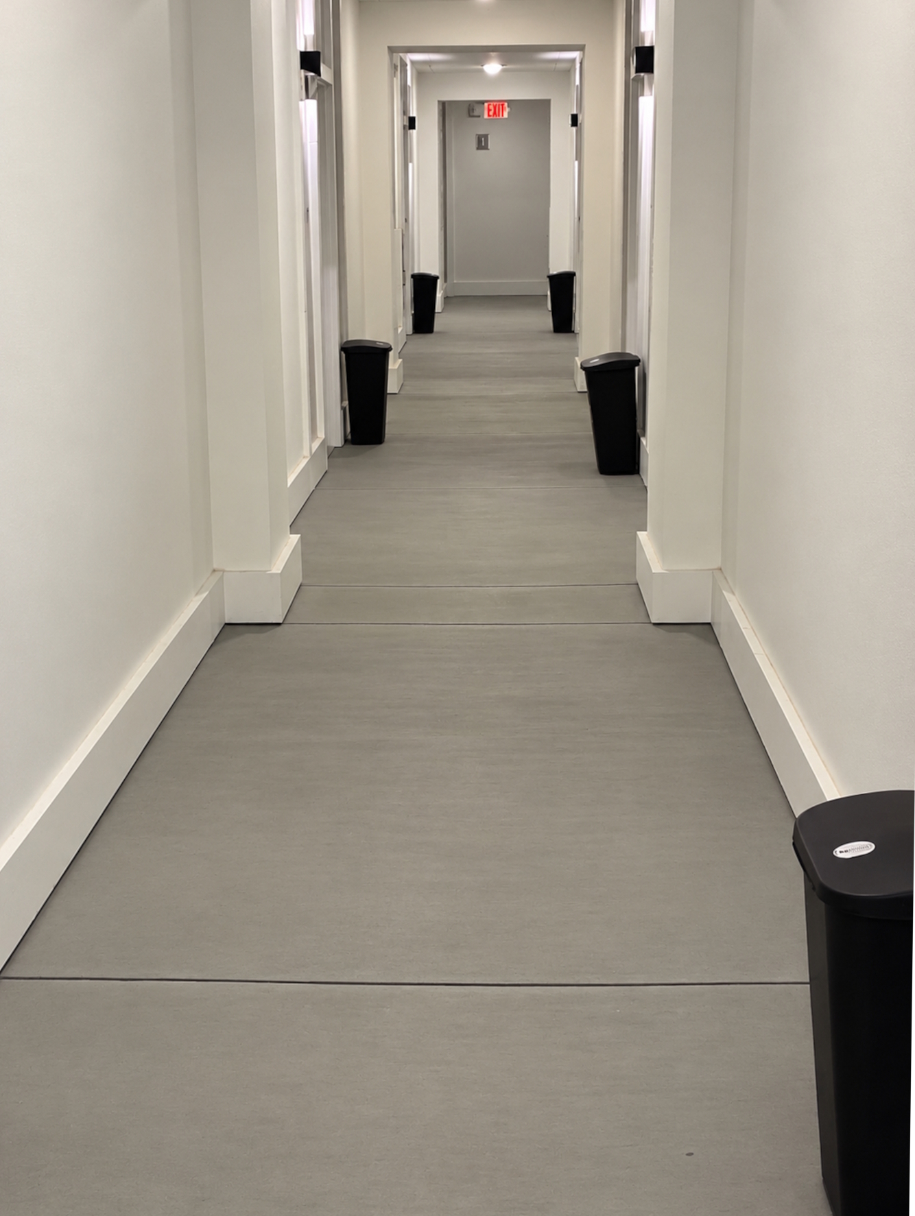 Trash bins set outside apartment doors along a corridor at night